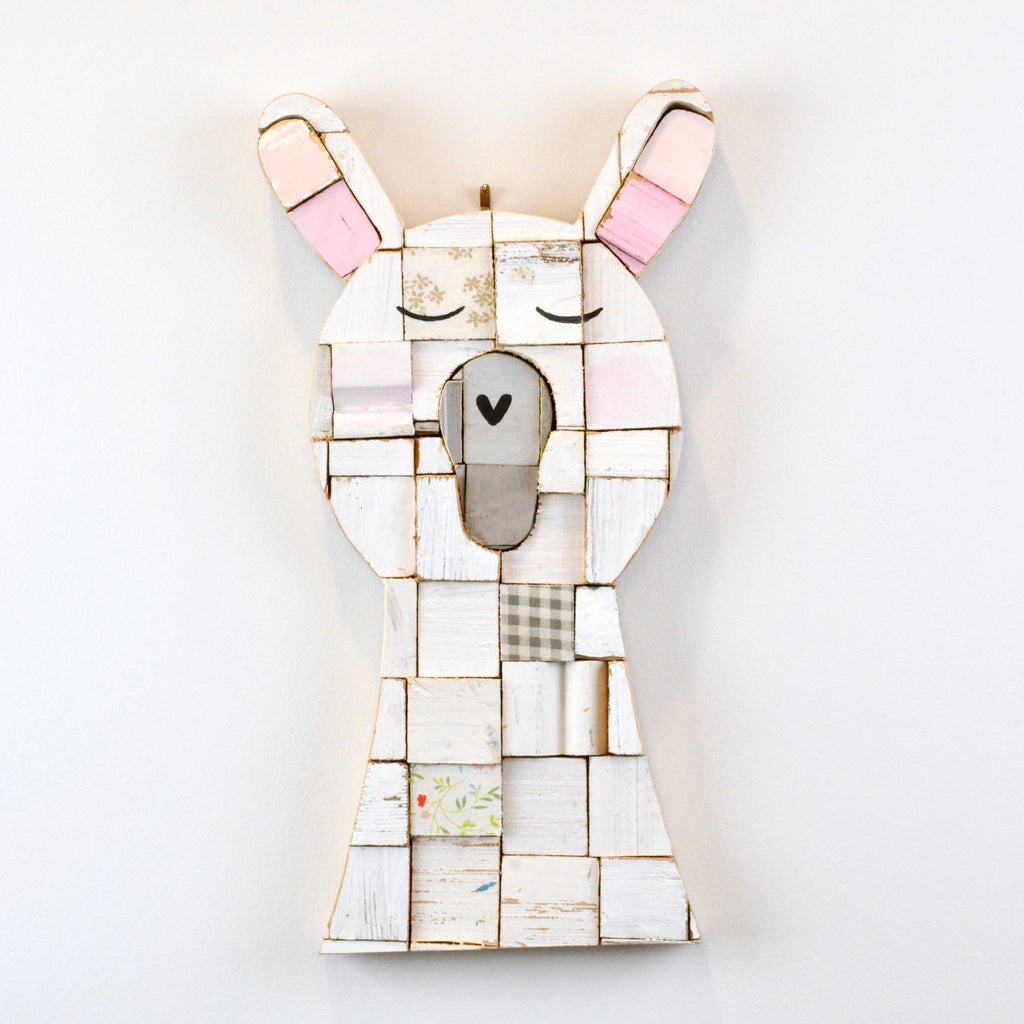 Portrait of a llama with closed eyes and a bit of attitude handmade using salvaged wood blocks in colours of whites and soft pinks re-assembled to create an art piece