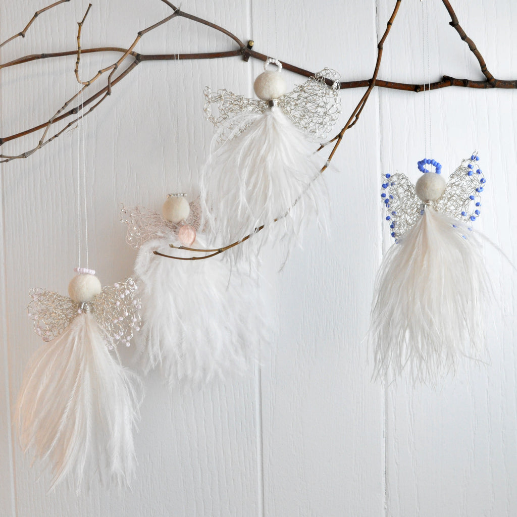 wire and feather angels hanging on a branch attached to a white wood panel wall