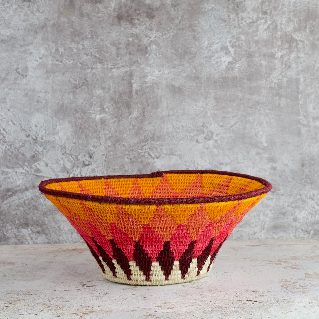 side view of a medium size hand woven sisal basket. diamond pattern. summer of love mixed colours of cream, mango,coral, fuscia, aubergine