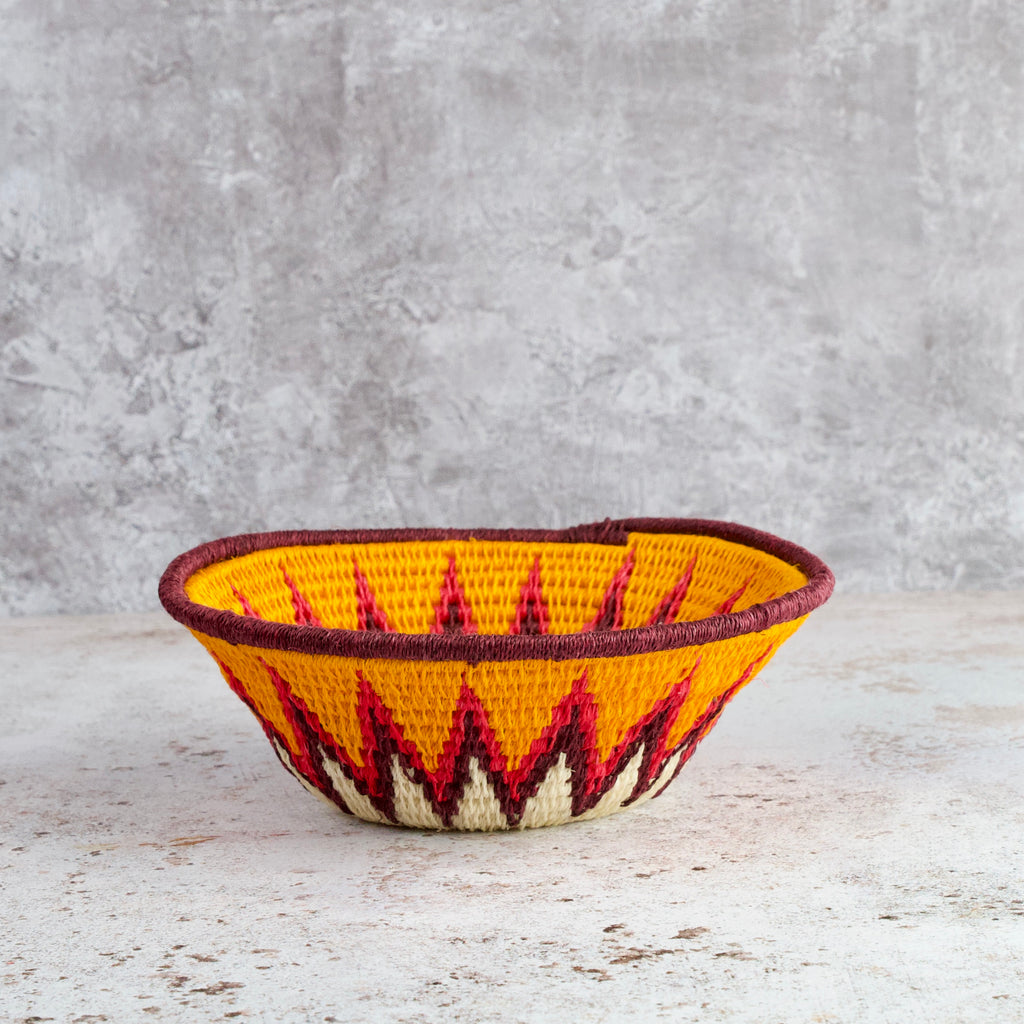 side view of small hand woven sisal basket. Protea pattern. summer of love mixed colours of cream, mango,coral, fuscia, aubergine
